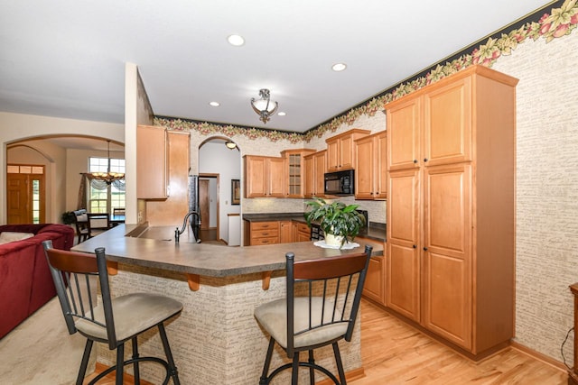 kitchen with light hardwood / wood-style flooring, backsplash, a breakfast bar, kitchen peninsula, and sink