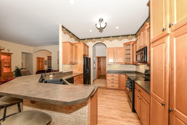 kitchen featuring a kitchen breakfast bar, black appliances, light hardwood / wood-style floors, kitchen peninsula, and sink