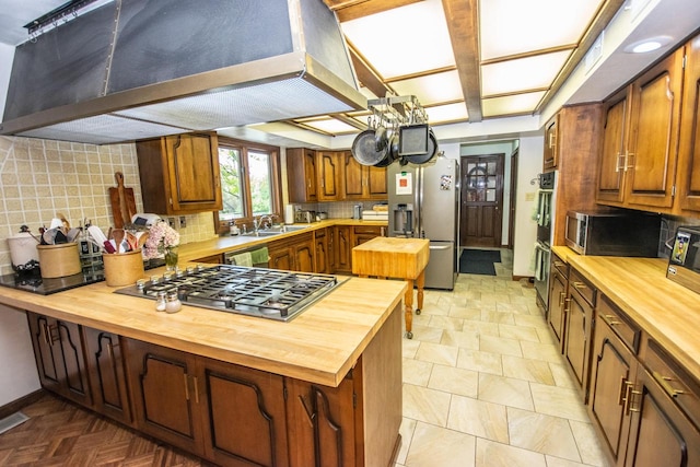 kitchen with appliances with stainless steel finishes, tasteful backsplash, kitchen peninsula, and butcher block countertops