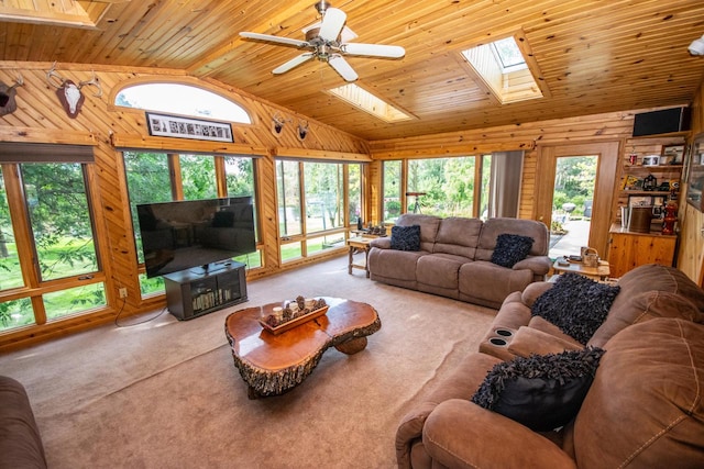 living room with high vaulted ceiling, a skylight, light colored carpet, ceiling fan, and wooden walls