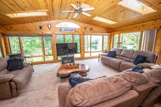 carpeted living area with wooden walls, ceiling fan, a wood stove, wood ceiling, and lofted ceiling with skylight