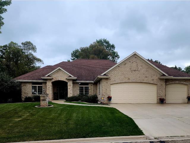 single story home featuring driveway, brick siding, an attached garage, and a front yard