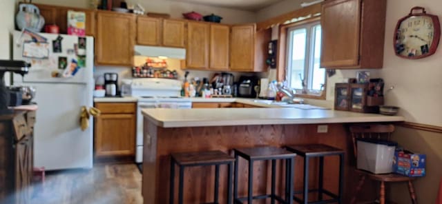 kitchen with a breakfast bar area, sink, white appliances, and kitchen peninsula