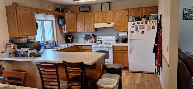 kitchen with white appliances, kitchen peninsula, sink, a breakfast bar area, and light hardwood / wood-style floors