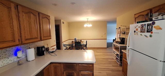 kitchen featuring white fridge, pendant lighting, a notable chandelier, light hardwood / wood-style floors, and kitchen peninsula