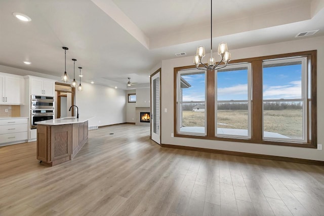 kitchen featuring sink, white cabinetry, decorative light fixtures, double oven, and a kitchen island with sink