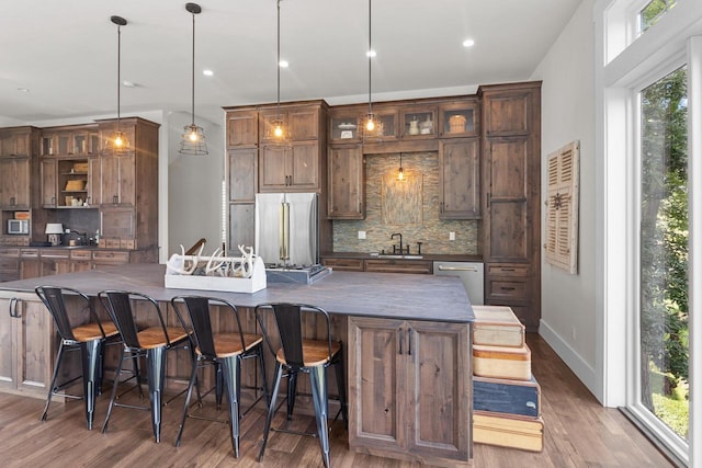 kitchen with backsplash, stainless steel appliances, sink, hanging light fixtures, and hardwood / wood-style flooring