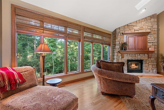 interior space with a fireplace, vaulted ceiling with skylight, a healthy amount of sunlight, and light hardwood / wood-style flooring