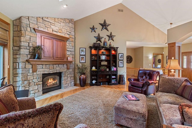 living room featuring a stone fireplace, high vaulted ceiling, decorative columns, and light hardwood / wood-style floors