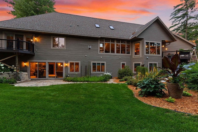 back house at dusk with a patio, a lawn, and a wooden deck