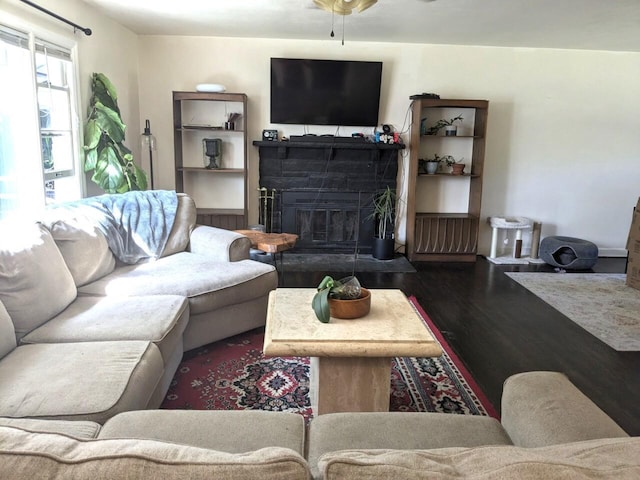 living room featuring ceiling fan, a stone fireplace, and dark hardwood / wood-style flooring