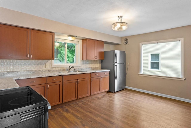 kitchen with light hardwood / wood-style flooring, electric range, sink, stainless steel fridge, and decorative backsplash