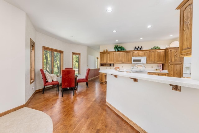 kitchen featuring baseboards, a breakfast bar, light wood-type flooring, light countertops, and white appliances