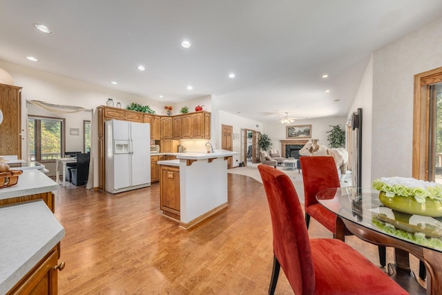 kitchen featuring white refrigerator with ice dispenser, open floor plan, a peninsula, a fireplace, and light wood finished floors