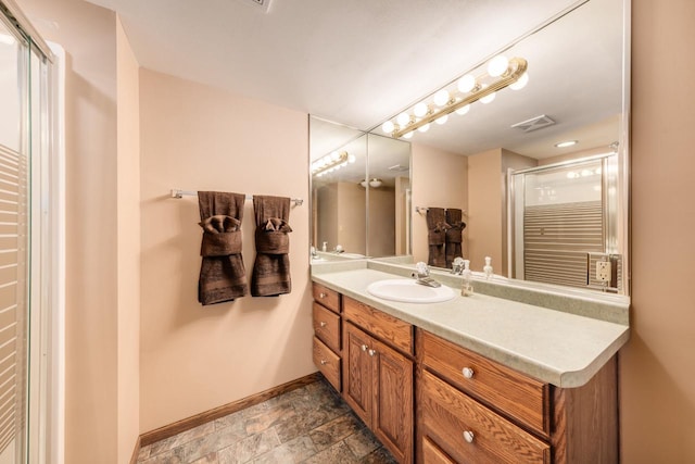 full bath featuring vanity, a shower with shower door, visible vents, baseboards, and stone finish floor