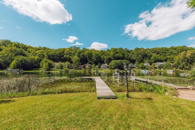 view of community with a forest view, a dock, a yard, and a water view