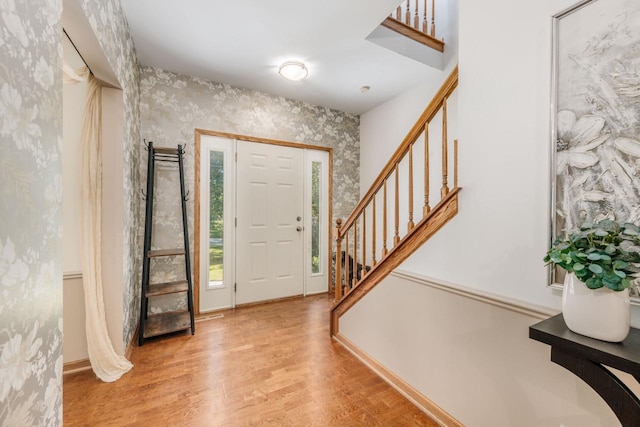 foyer entrance featuring wallpapered walls, stairs, baseboards, and wood finished floors