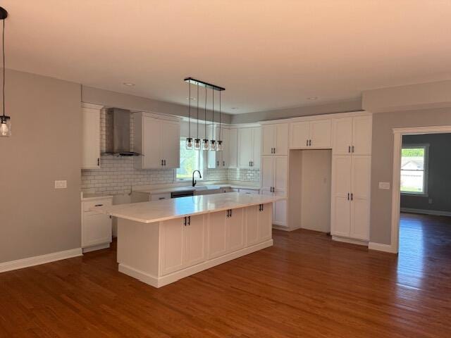 kitchen with white cabinetry, dark hardwood / wood-style flooring, a center island, decorative light fixtures, and wall chimney range hood