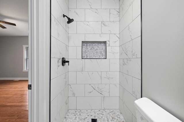 bathroom with a tile shower, toilet, hardwood / wood-style floors, and ceiling fan