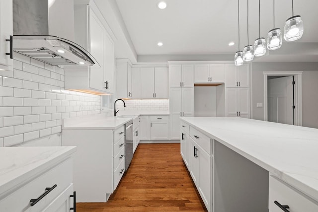 kitchen featuring light stone counters, white cabinetry, hanging light fixtures, wall chimney exhaust hood, and hardwood / wood-style floors