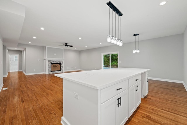 kitchen featuring a center island, white cabinetry, hanging light fixtures, light hardwood / wood-style flooring, and a stone fireplace