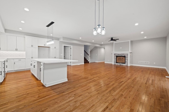 kitchen featuring light wood-type flooring, decorative light fixtures, white cabinetry, a fireplace, and ceiling fan with notable chandelier