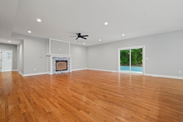 unfurnished living room with ceiling fan, a stone fireplace, and light hardwood / wood-style flooring