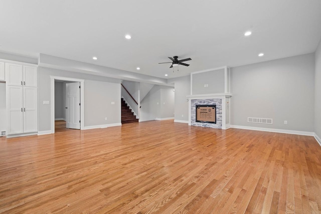 unfurnished living room with ceiling fan, a stone fireplace, and light hardwood / wood-style floors