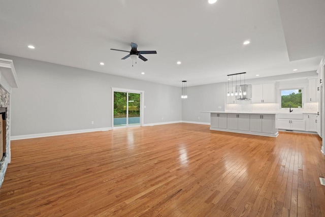 unfurnished living room featuring light wood-type flooring, ceiling fan, and a stone fireplace