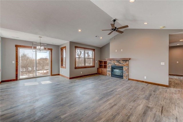 unfurnished living room with lofted ceiling, a healthy amount of sunlight, ceiling fan with notable chandelier, and a stone fireplace