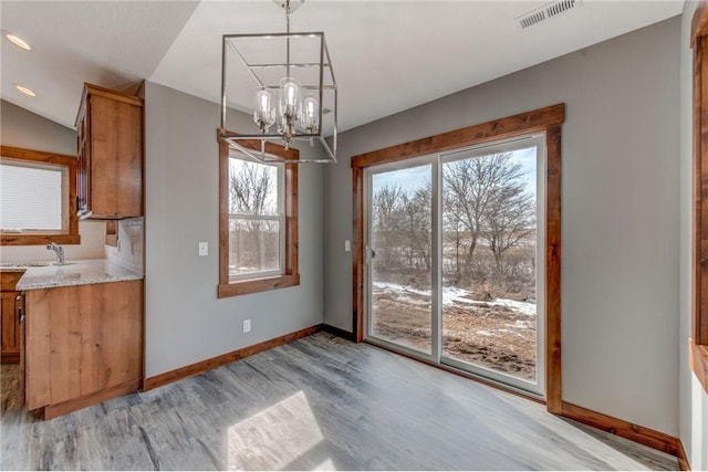 unfurnished dining area with light wood-type flooring, lofted ceiling, a notable chandelier, and sink