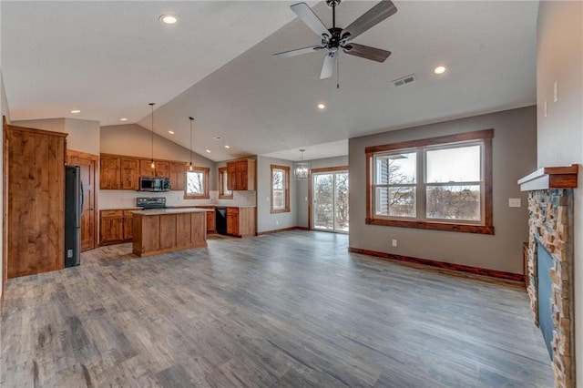 unfurnished living room featuring light hardwood / wood-style flooring, ceiling fan, a stone fireplace, and vaulted ceiling