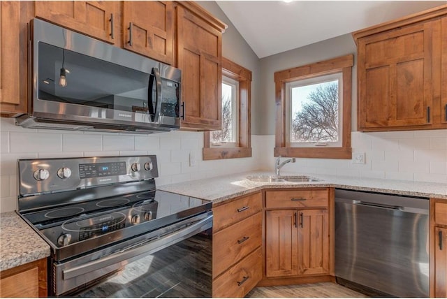 kitchen with appliances with stainless steel finishes, vaulted ceiling, light hardwood / wood-style flooring, and light stone countertops