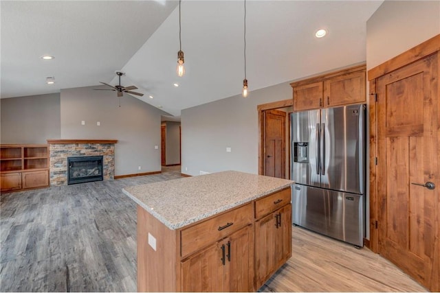 kitchen with vaulted ceiling, a fireplace, stainless steel refrigerator with ice dispenser, ceiling fan, and light stone counters