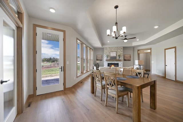 1629 N Honeysuckle Cir, De Pere, WI 54115 - dining room featuring a stone fireplace, light wood finished floors, an inviting chandelier, and a raised ceiling