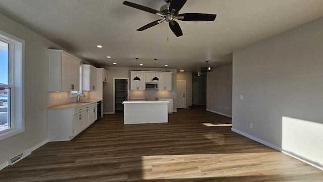 kitchen with visible vents, a sink, stainless steel microwave, dark wood-style floors, and a center island