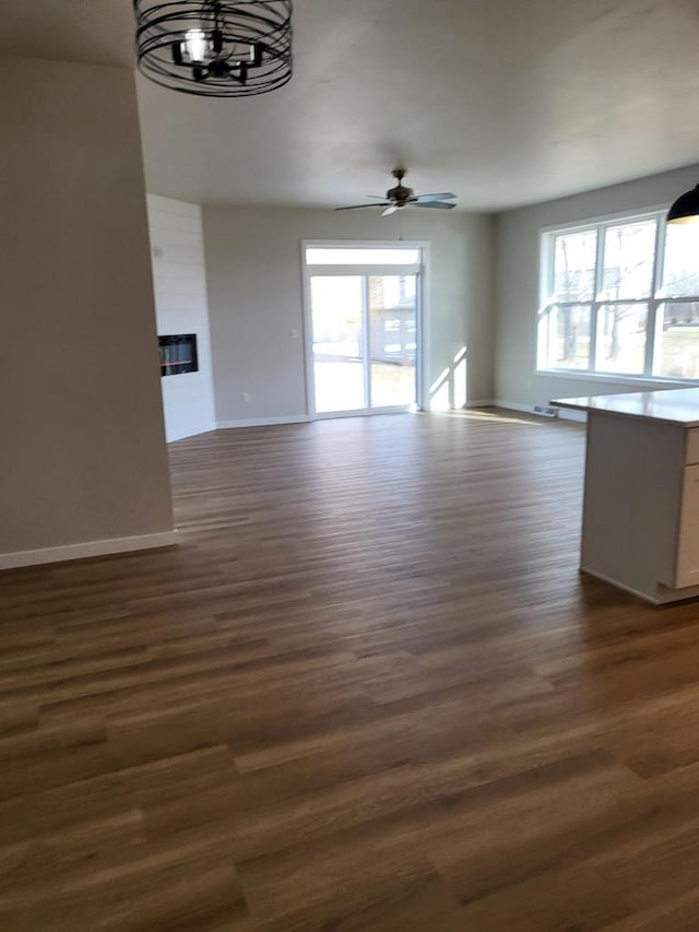 unfurnished living room featuring baseboards, plenty of natural light, and dark wood-style flooring