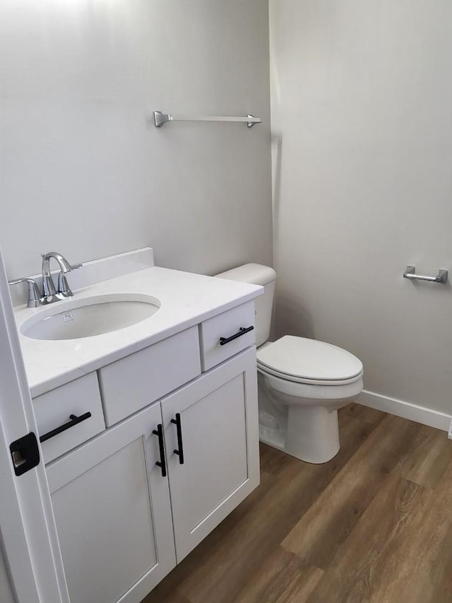 half bath with toilet, vanity, baseboards, and wood finished floors