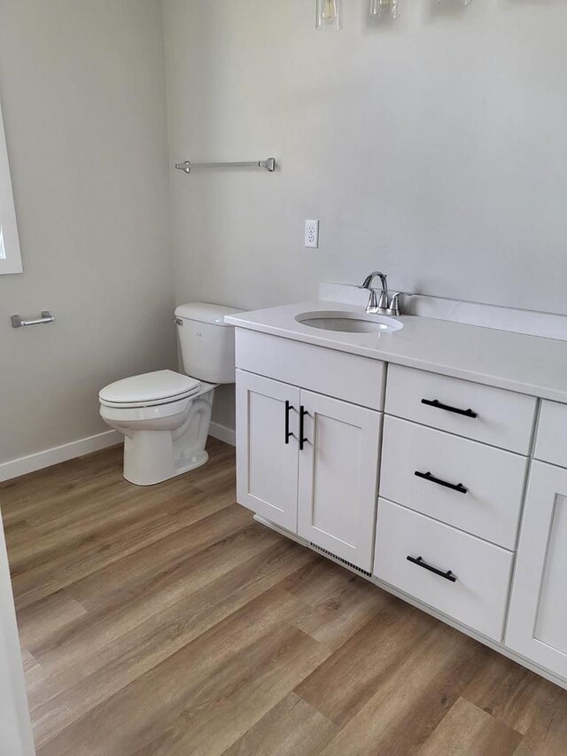 half bath with vanity, toilet, wood finished floors, and baseboards