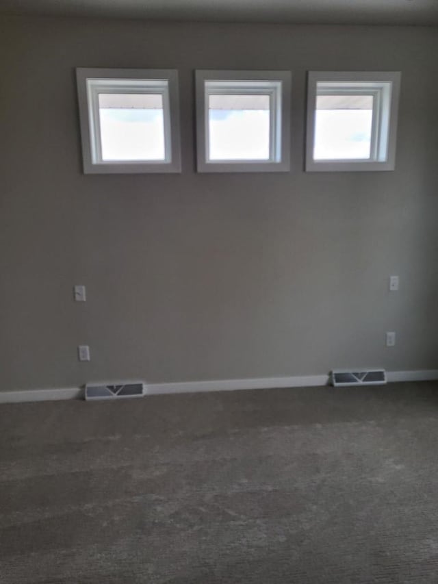 spare room with dark colored carpet, visible vents, and plenty of natural light