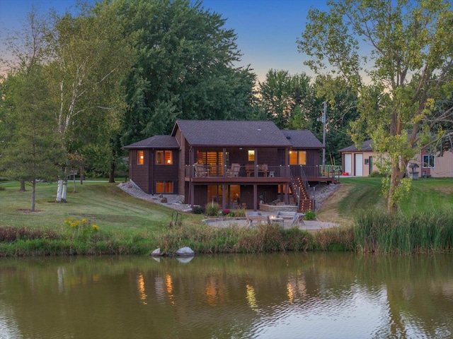 back house at dusk featuring a lawn and a deck with water view