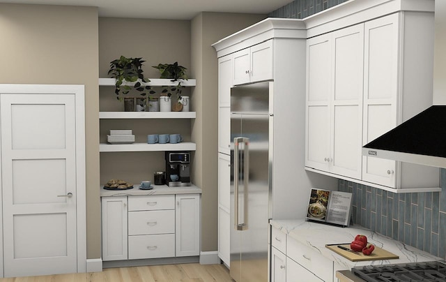 kitchen featuring decorative backsplash, light stone counters, white cabinets, stainless steel built in refrigerator, and light hardwood / wood-style flooring