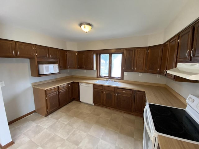 kitchen featuring under cabinet range hood, a sink, white appliances, light countertops, and baseboards