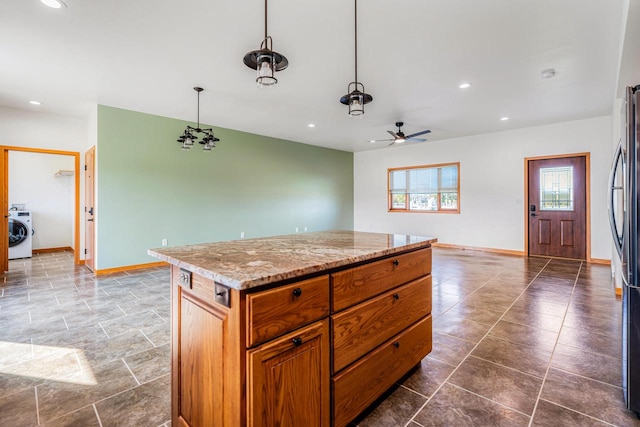 kitchen featuring washer / dryer, light stone countertops, a center island, ceiling fan, and pendant lighting