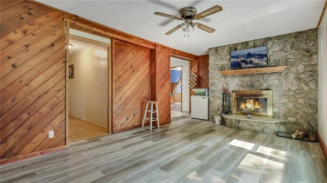 unfurnished living room with a ceiling fan, wooden walls, wood finished floors, and a fireplace