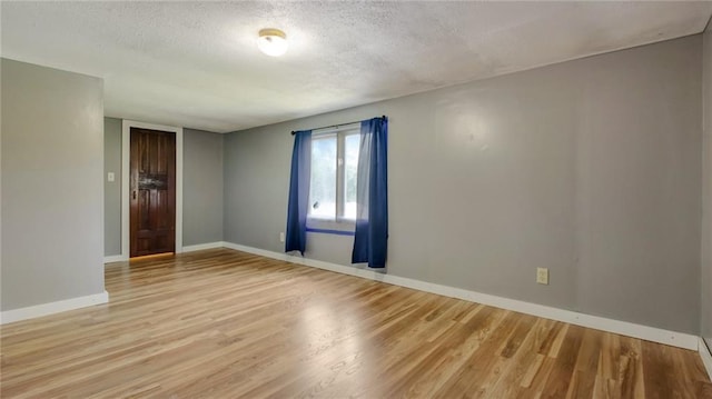 empty room with light wood finished floors, a textured ceiling, and baseboards