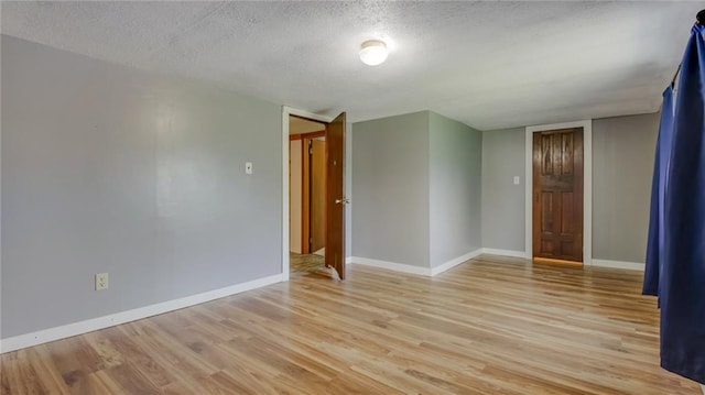 empty room featuring light wood-type flooring, baseboards, and a textured ceiling