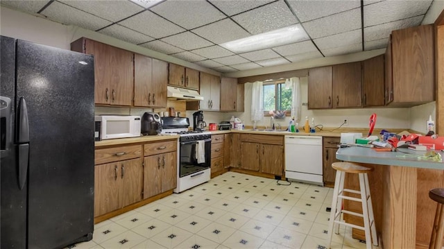 kitchen with white appliances, brown cabinetry, light floors, a peninsula, and under cabinet range hood