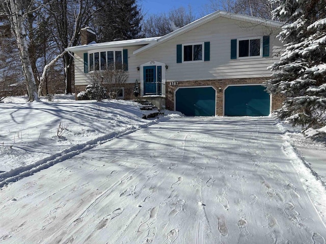 split foyer home featuring brick siding, driveway, a chimney, and a garage