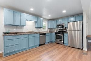 kitchen with blue cabinets, light wood-type flooring, sink, and appliances with stainless steel finishes